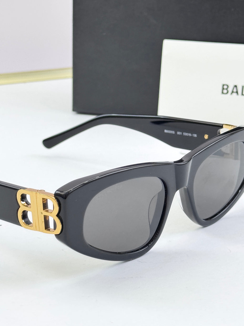 Matte black cat-eye sunglasses with dark lenses and gold B logo at temple