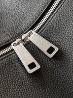 Black leather bag with two silver zipper pulls and rectangular logo tabs