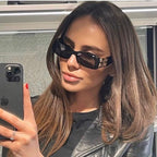 Balenciaga sunglasses with black frames and gold B logo temples, worn in profile