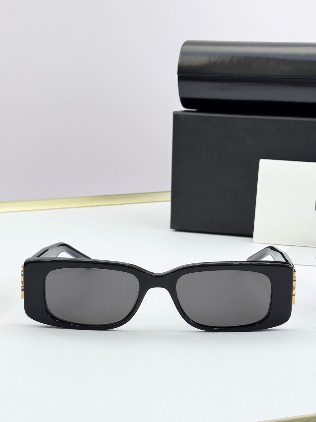 Balenciaga sunglasses, matte black frames with gold B logo accents, dark lenses