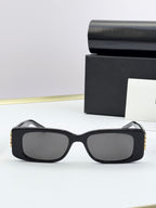Balenciaga sunglasses, matte black frames with gold B logo accents, dark lenses