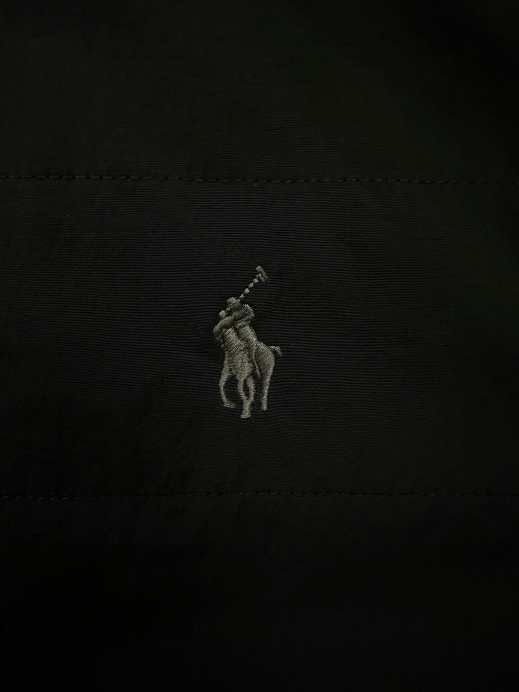 Embroidered polo rider logo on black fabric.