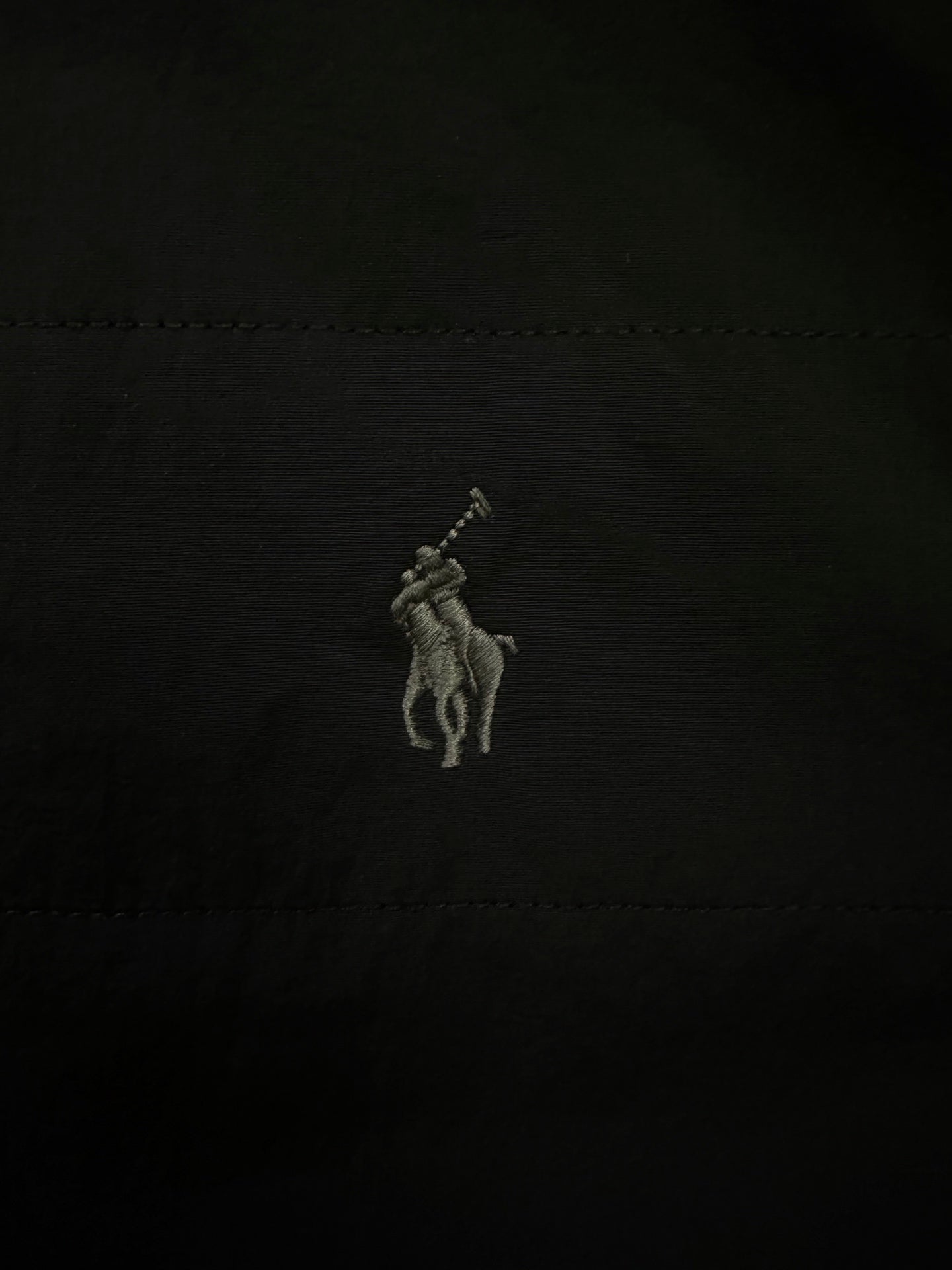 Embroidered polo rider logo on black fabric.