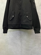 Black bomber jacket with snap-flap pockets and ribbed cuffs, front lower view.