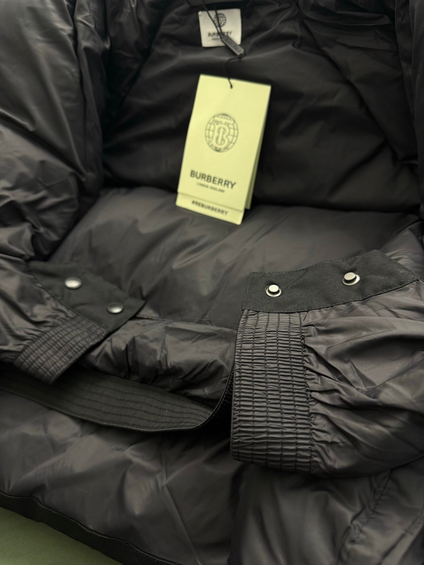Black puffer jacket with Burberry hang tag and snap-button cuff details