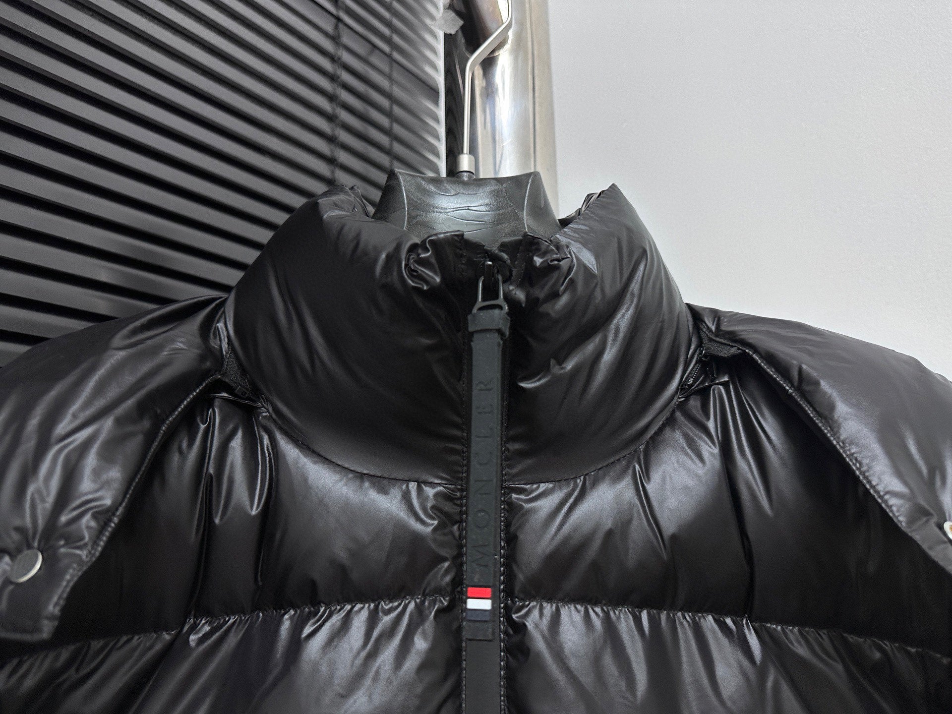 Black long puffer jacket with high collar and center zipper, snap hood detail