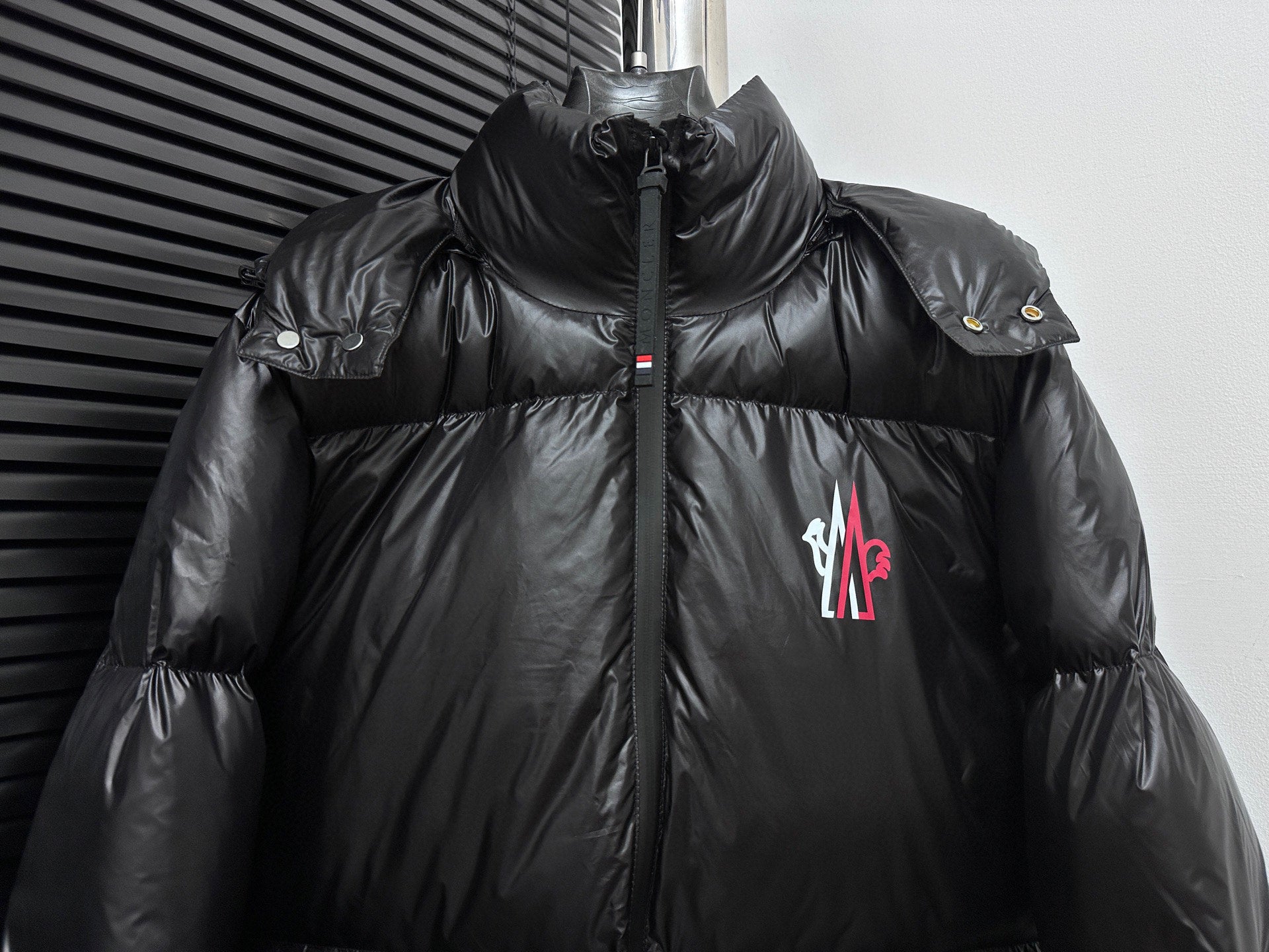 Black long puffer jacket front view with zipper, shoulder snap badge, chest logo