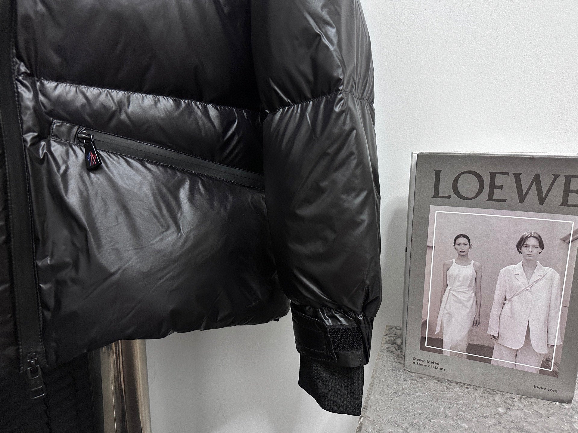 Black puffer jacket side view with zip pocket and ribbed elastic sleeve hem