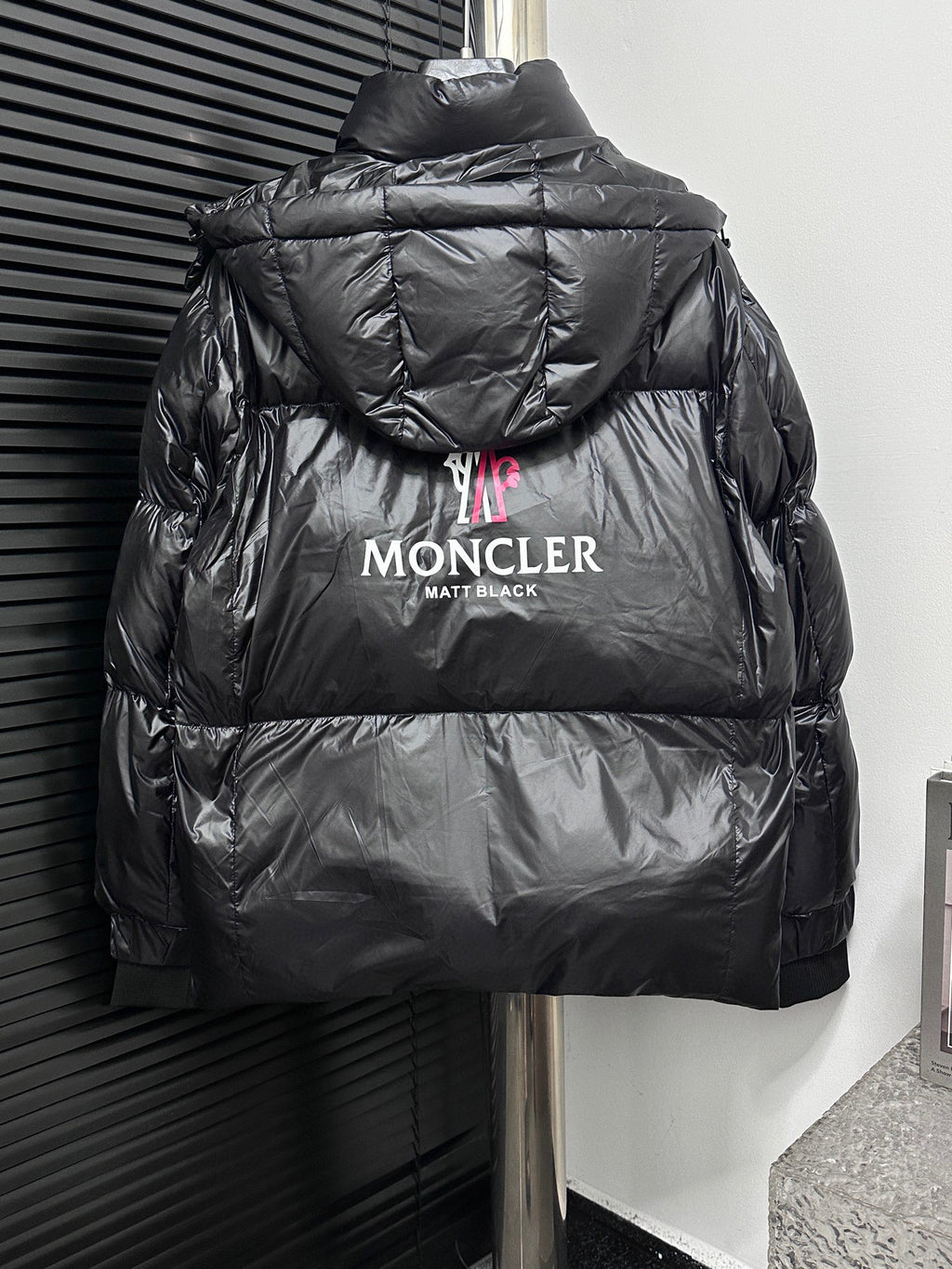 Black long puffer jacket back view with hood, “MONCLER” logo and text