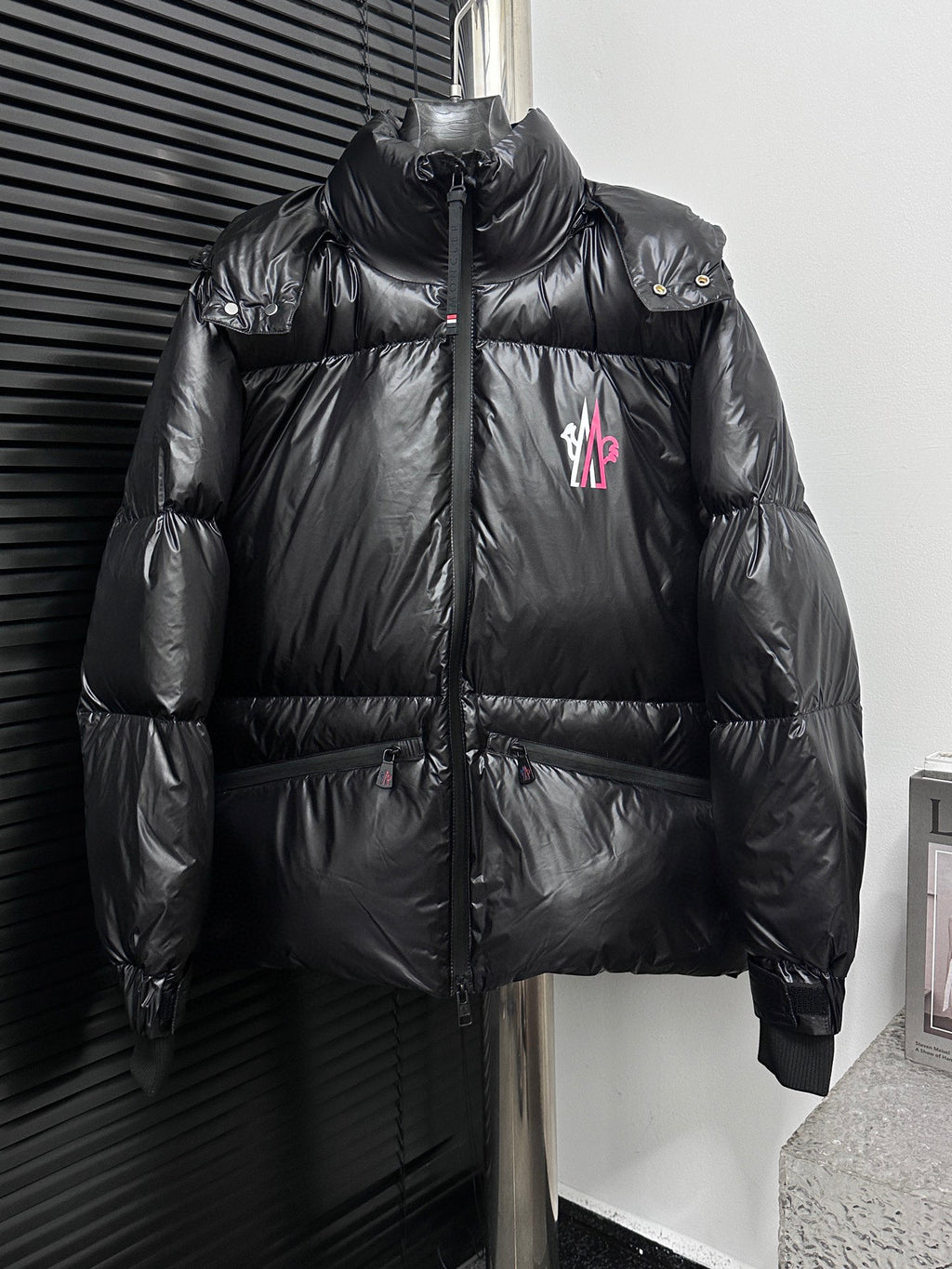 Black long puffer jacket, full-zip front, stand collar, chest logo patch