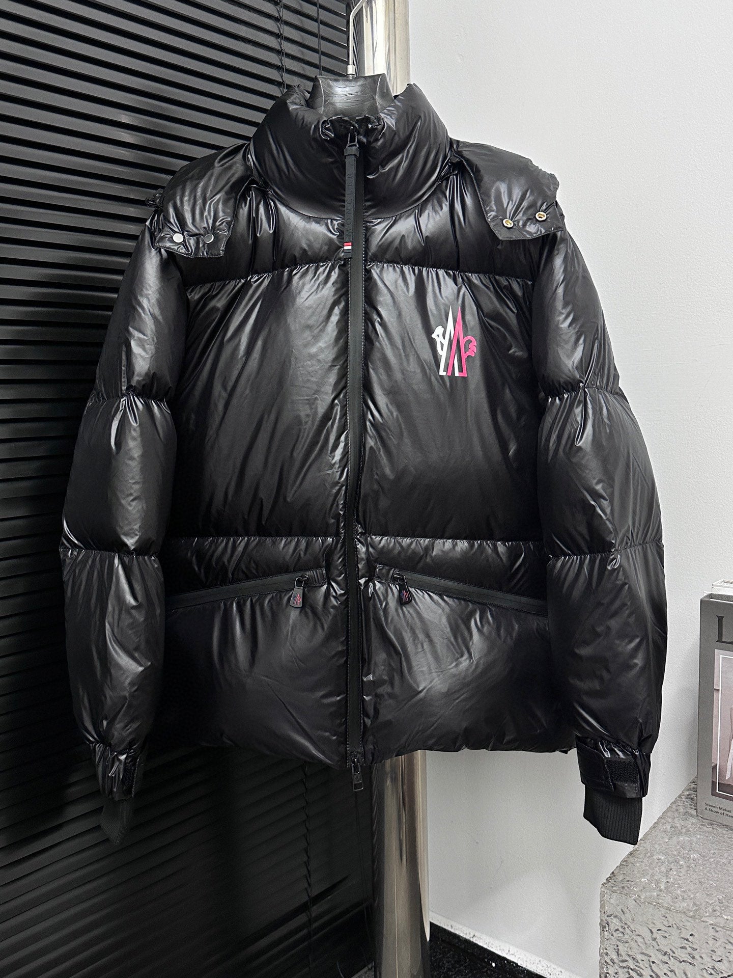 Black long puffer jacket, full-zip front, stand collar, chest logo patch
