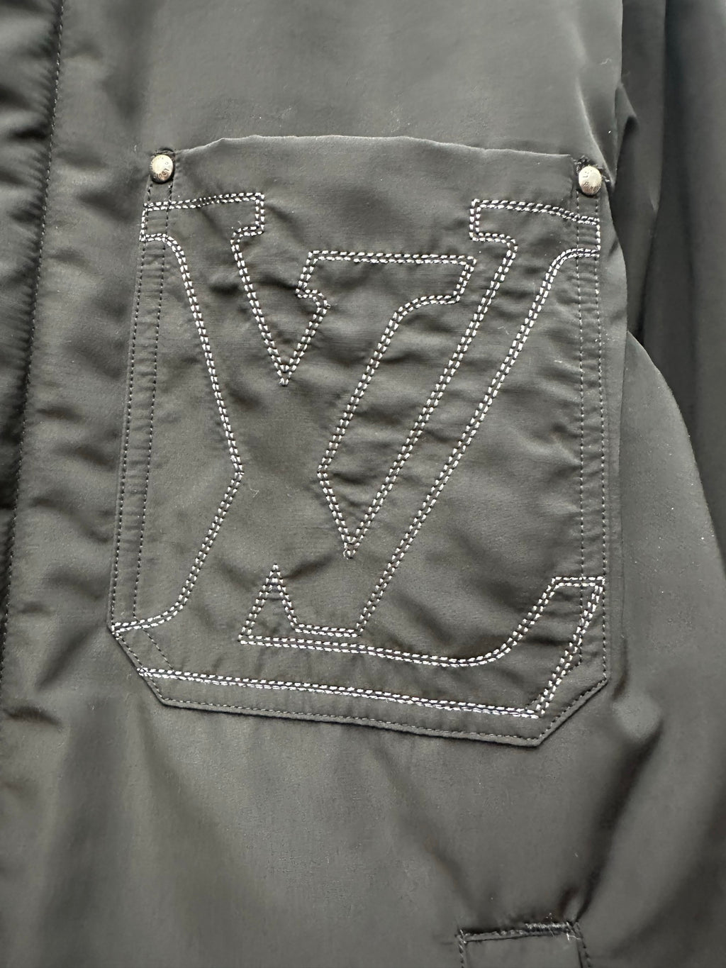 Chest logo pocket on dark green puffer jacket, outlined with stitched pattern
