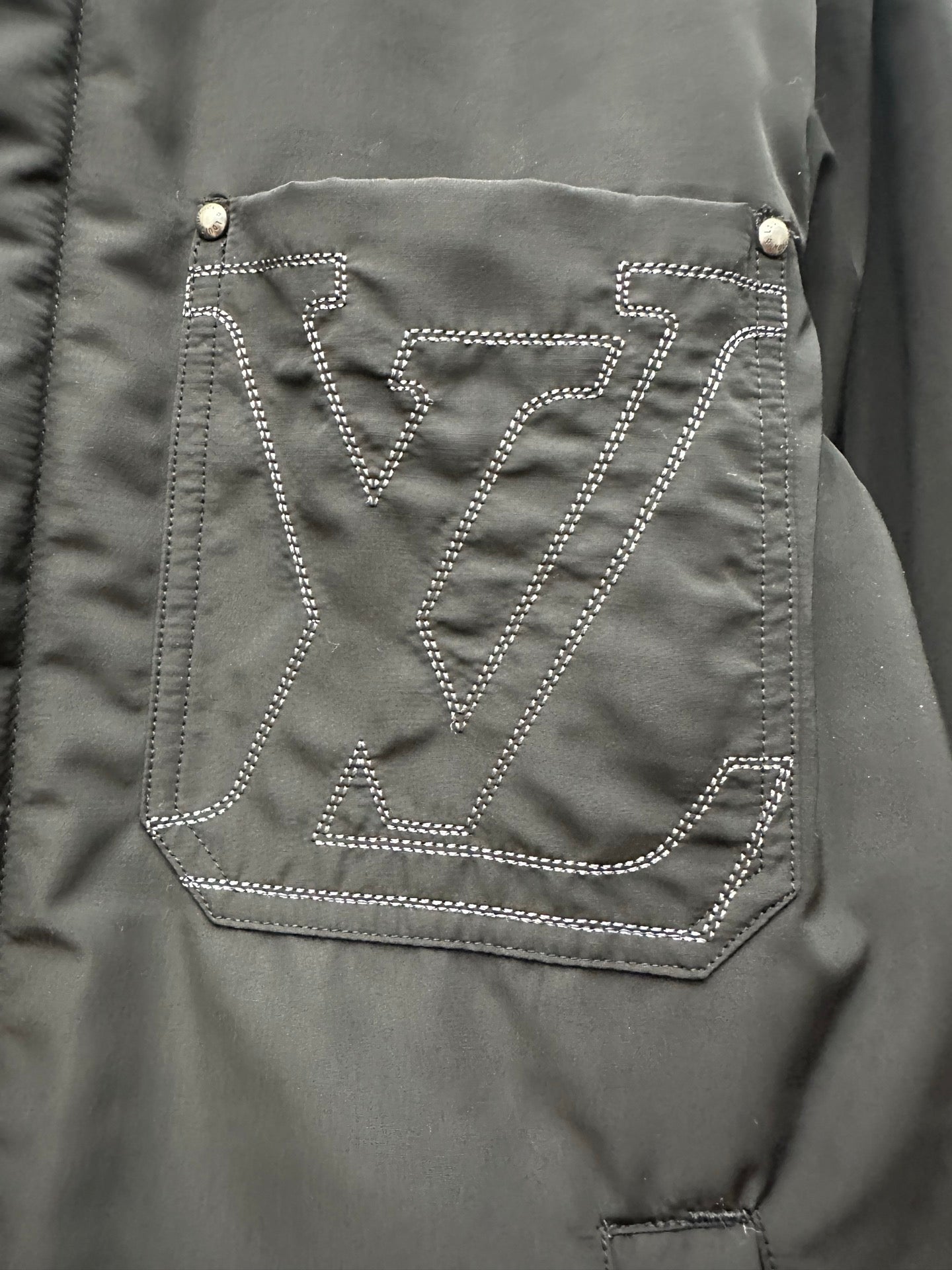 Chest logo pocket on dark green puffer jacket, outlined with stitched pattern