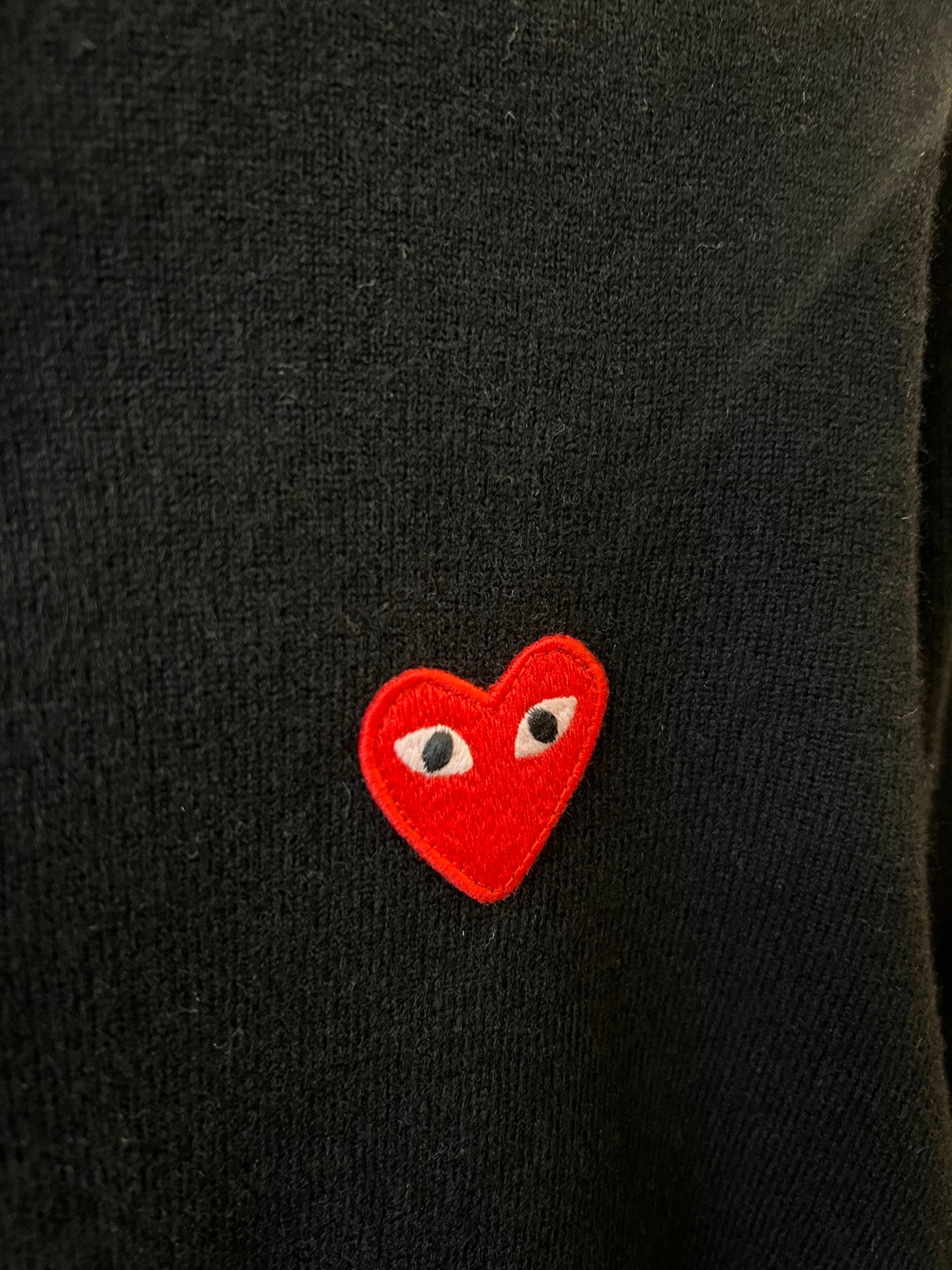 Embroidered red heart logo patch on Amiri dark knit cardigan.