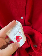 Red knit cardigan with round button and care label tag held by hand