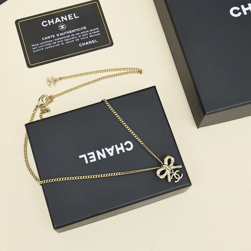 Gold-tone chain necklace with bow charm, shown on black gift box