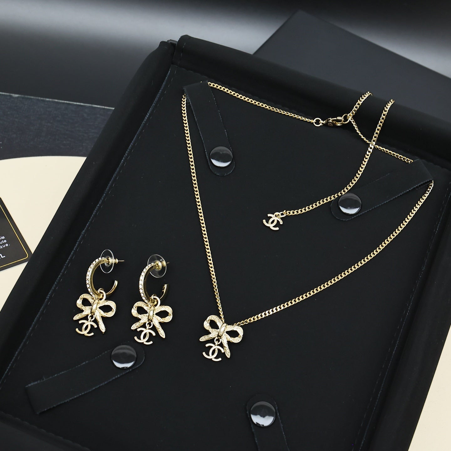 Gold-tone bow pendant necklace and matching earrings on black jewelry box