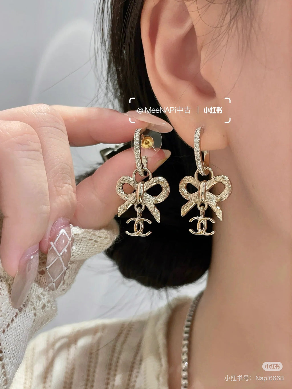 Gold-tone dangling earrings with rhinestone hoop and bow Chanel charm on ear