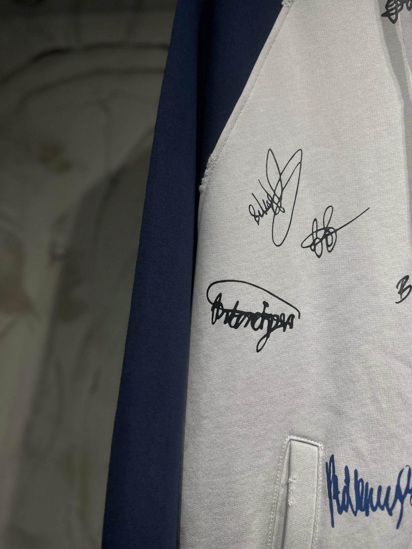 White hoodie front panel with black signature embroidery near a side seam