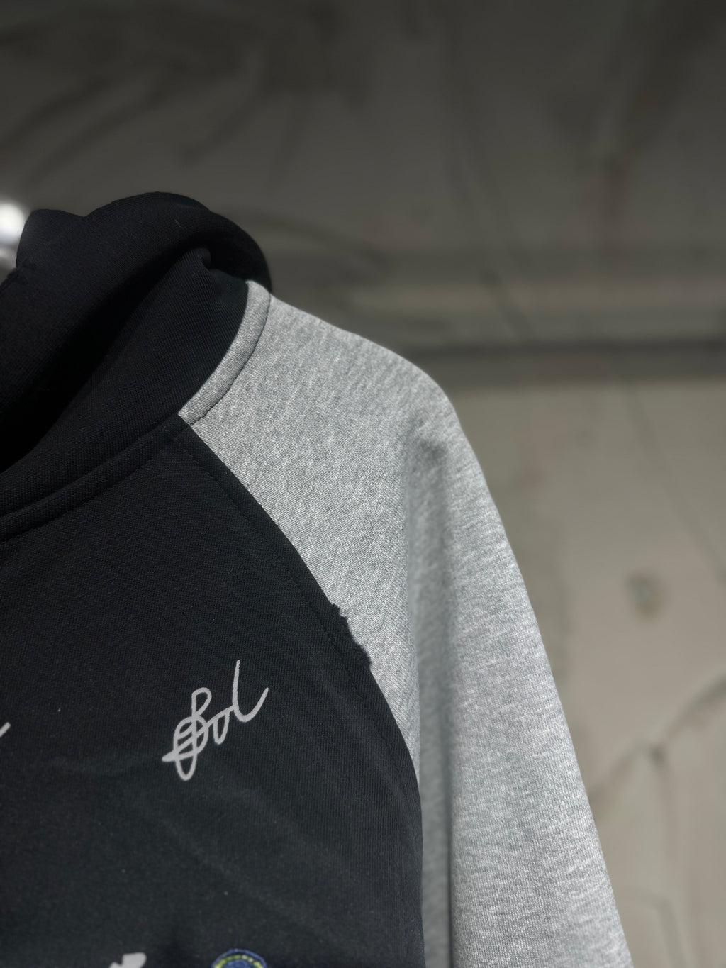 Two-tone hoodie front detail; black fabric with white script logo on the chest