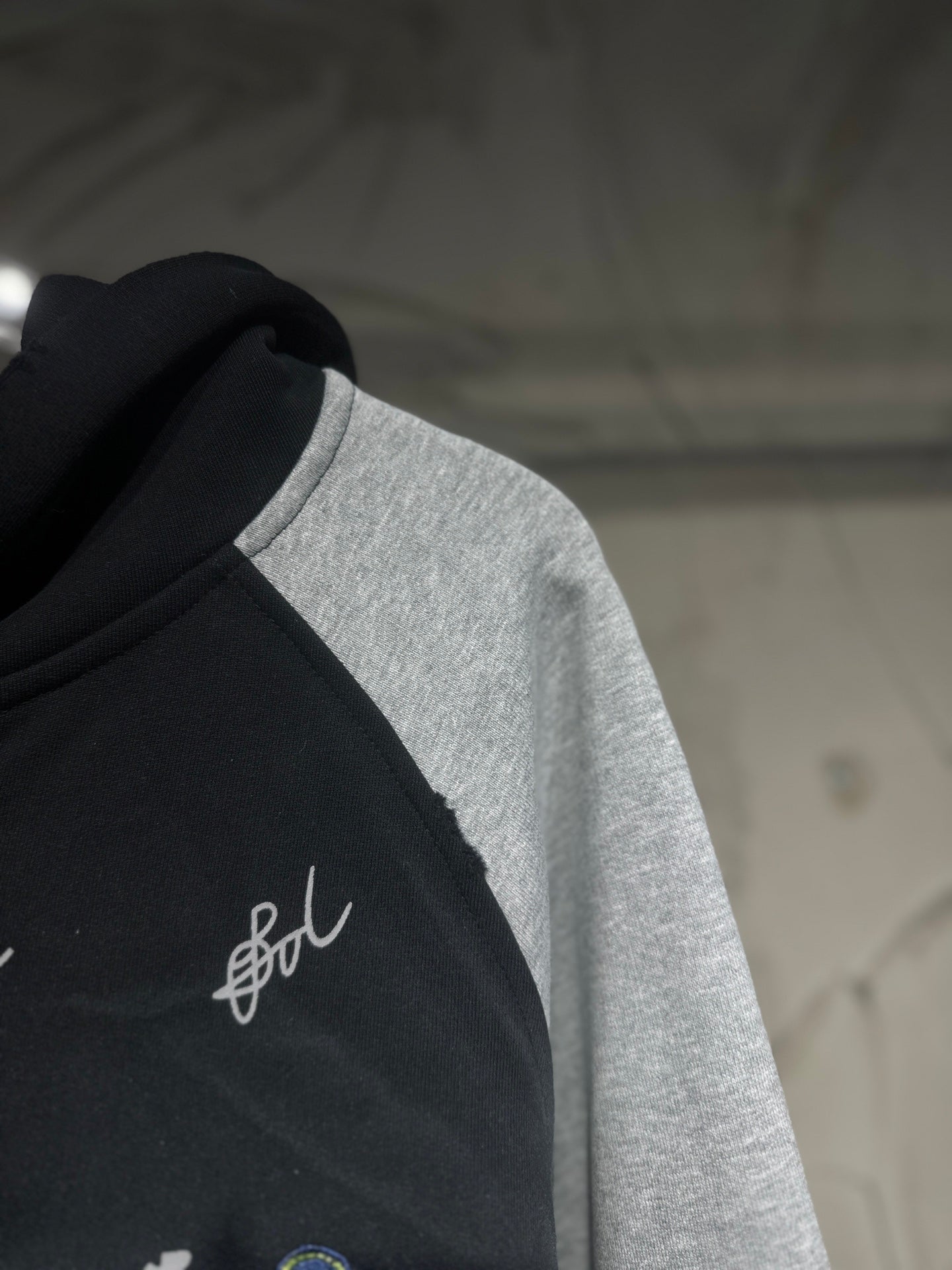 Two-tone hoodie front detail; black fabric with white script logo on the chest