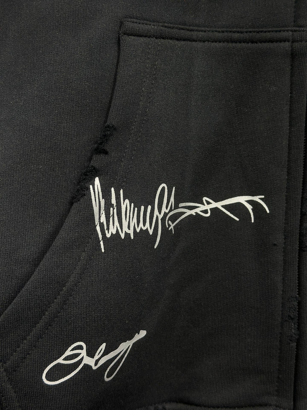 Black hoodie fabric with white script logo print and visible stitched seam
