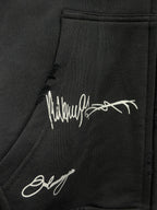 Black hoodie fabric with white script logo print and visible stitched seam