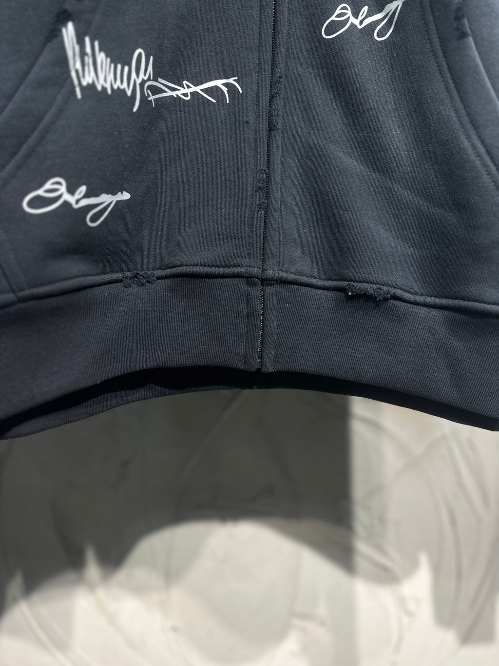Black zip-up hoodie front; white script graphics across the chest and zipper center