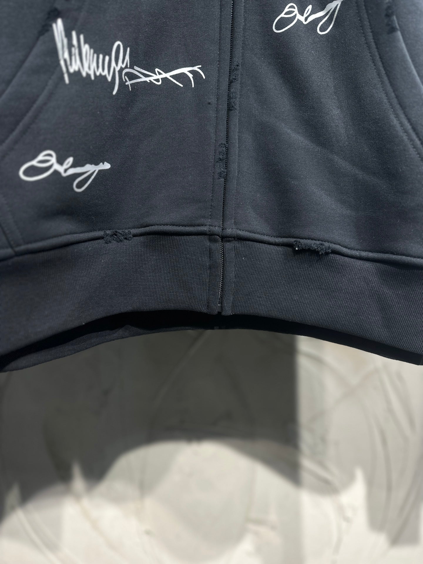 Black zip-up hoodie front; white script graphics across the chest and zipper center
