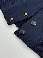 Navy monogram bomber jacket cuff with gold snap buttons and ribbed knit trim.