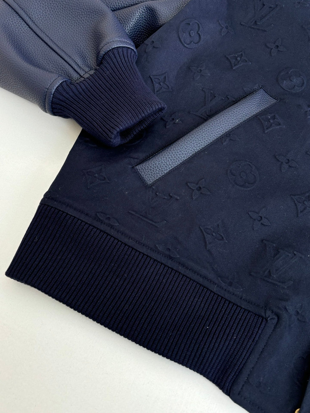 Navy bomber jacket detail: ribbed cuff and hem with snap button placket.