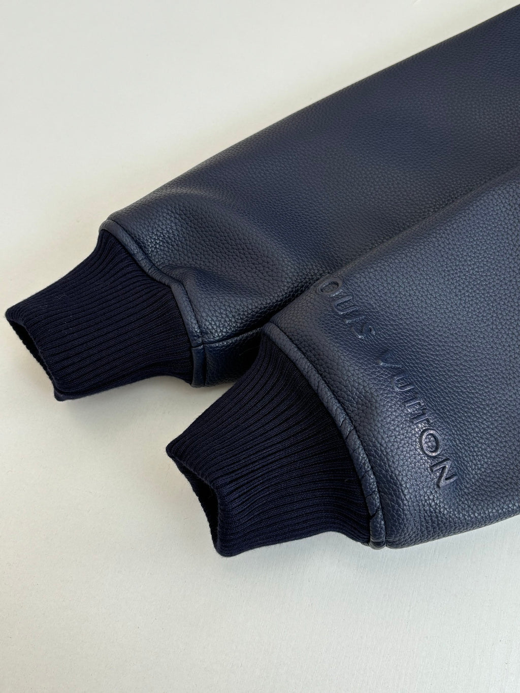 Navy ribbed sleeve cuff with embossed lettering on textured jacket trim.