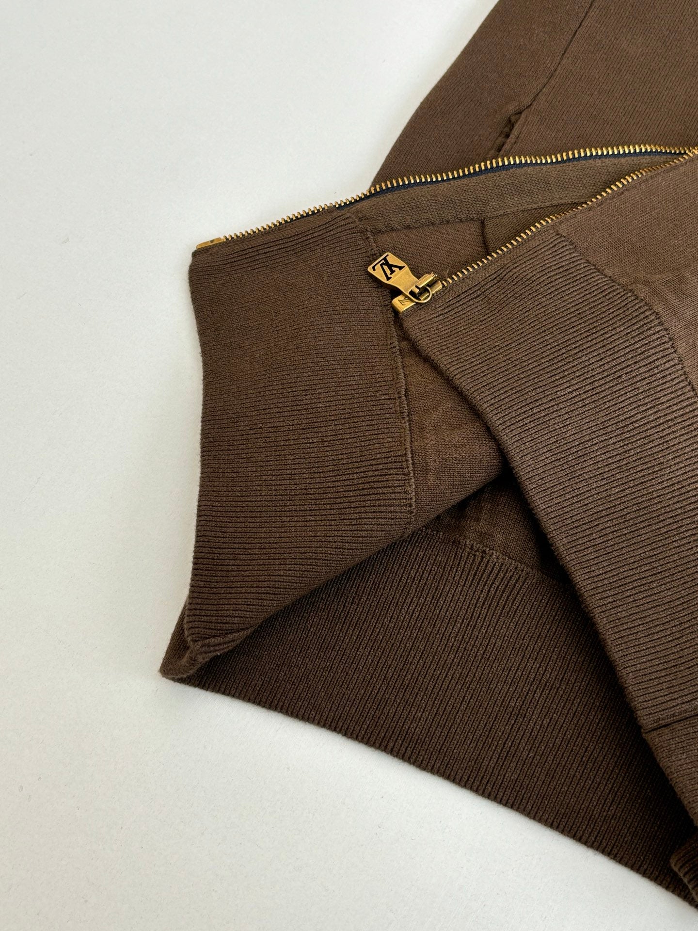 Brown jacket side seam with gold zipper track and small logo zipper pull
