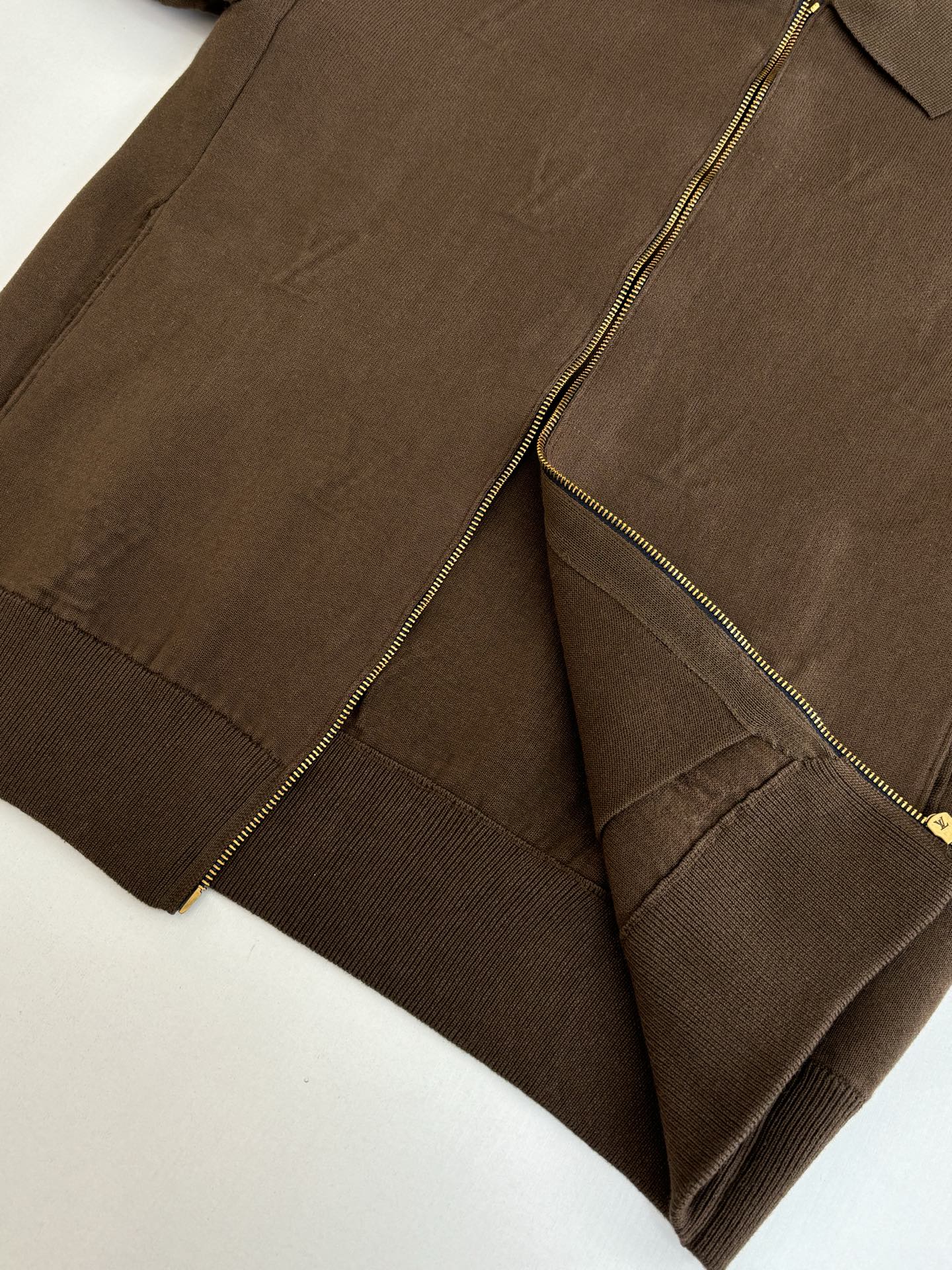 Brown jacket close-up showing front zipper, stitched panels, and ribbed hem