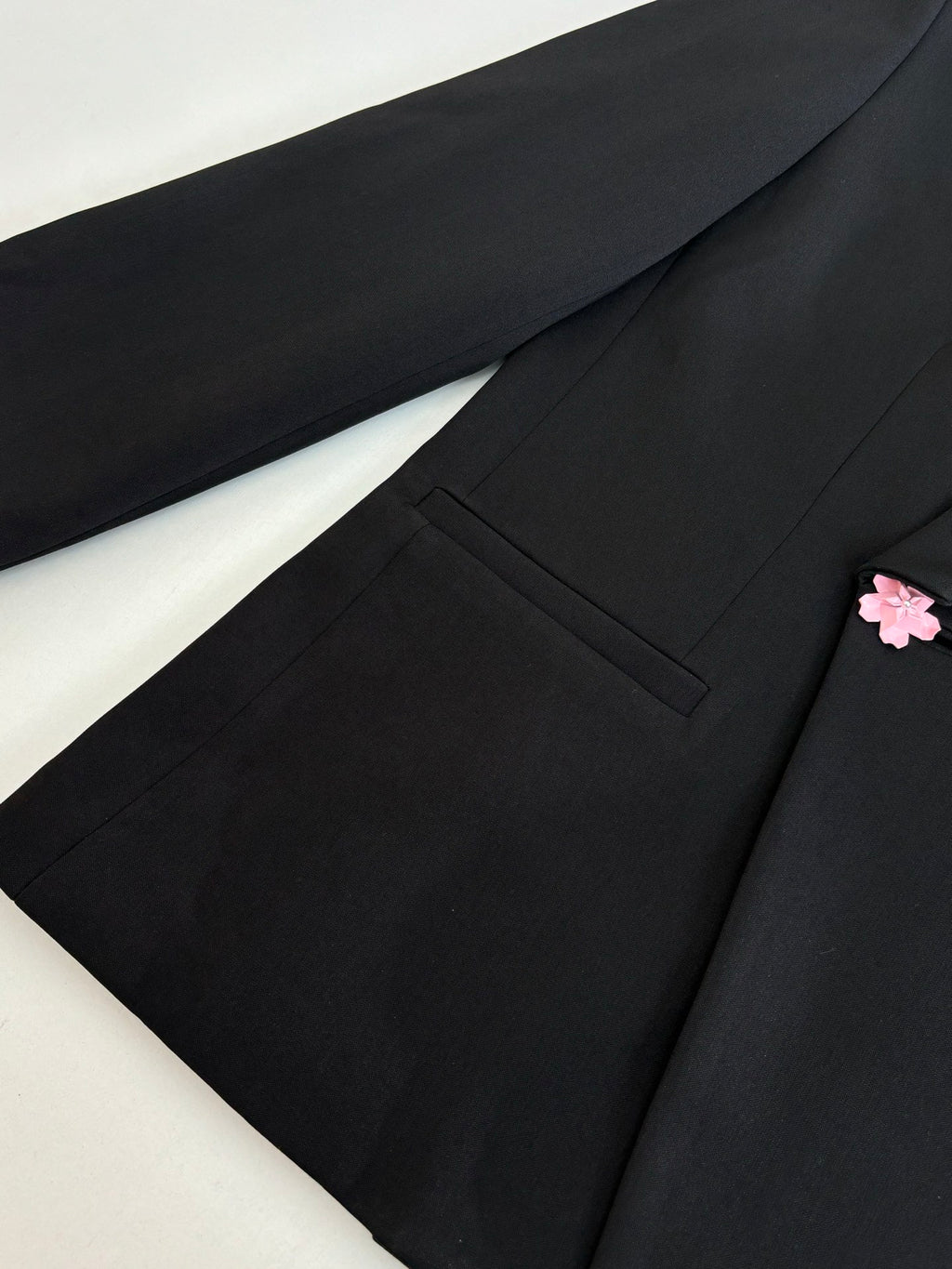 Black long blazer jacket close-up of front panel, pocket, and pink flower detail.