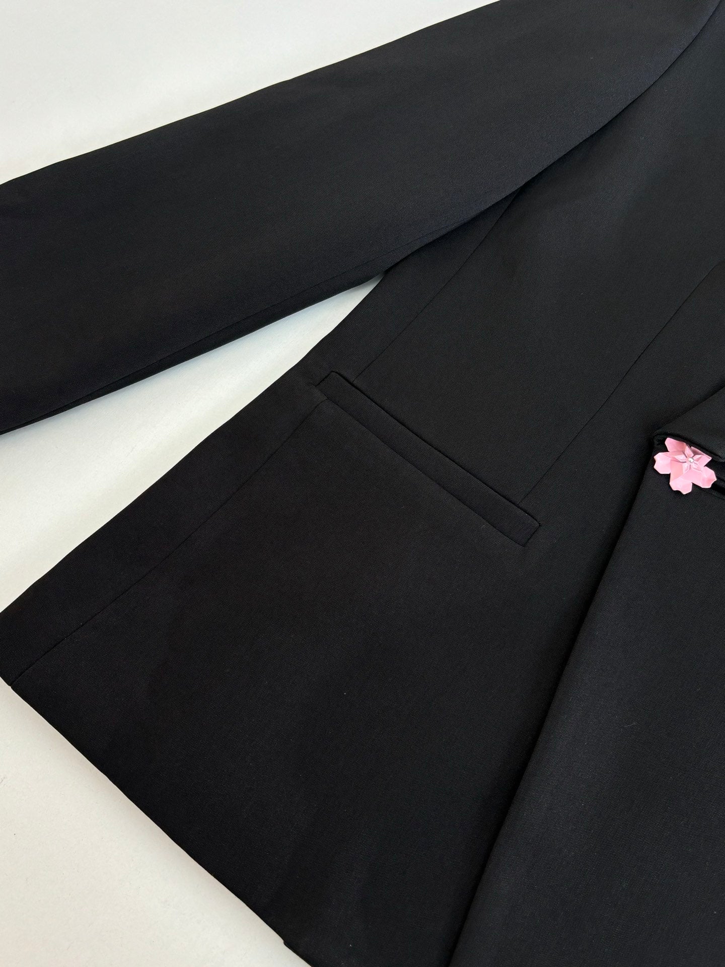 Black long blazer jacket close-up of front panel, pocket, and pink flower detail.