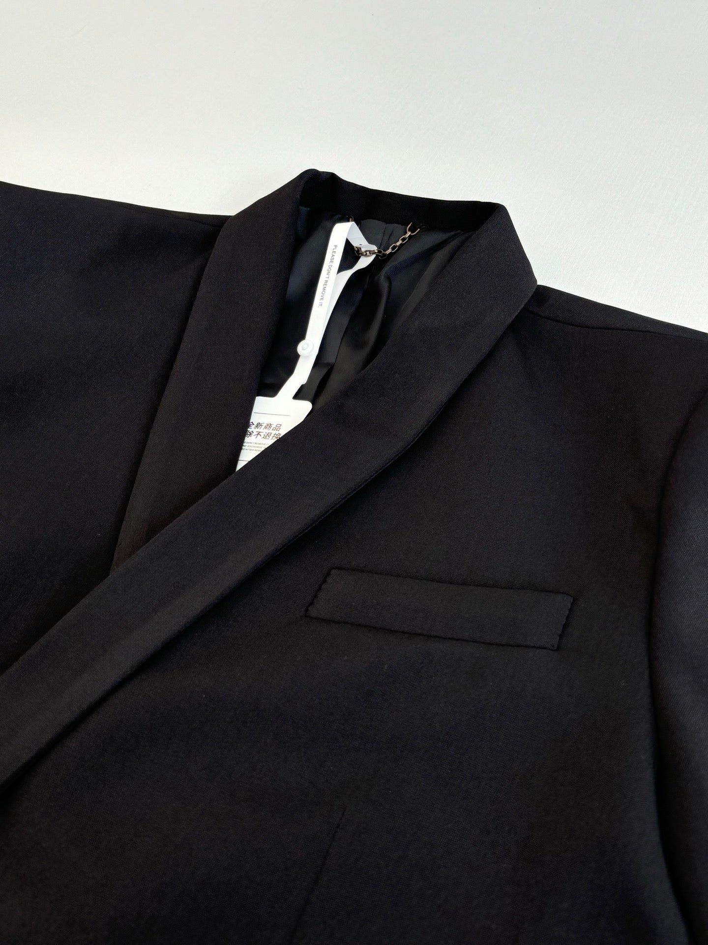 Black long blazer jacket close-up of lapel and front pocket, with inner label.