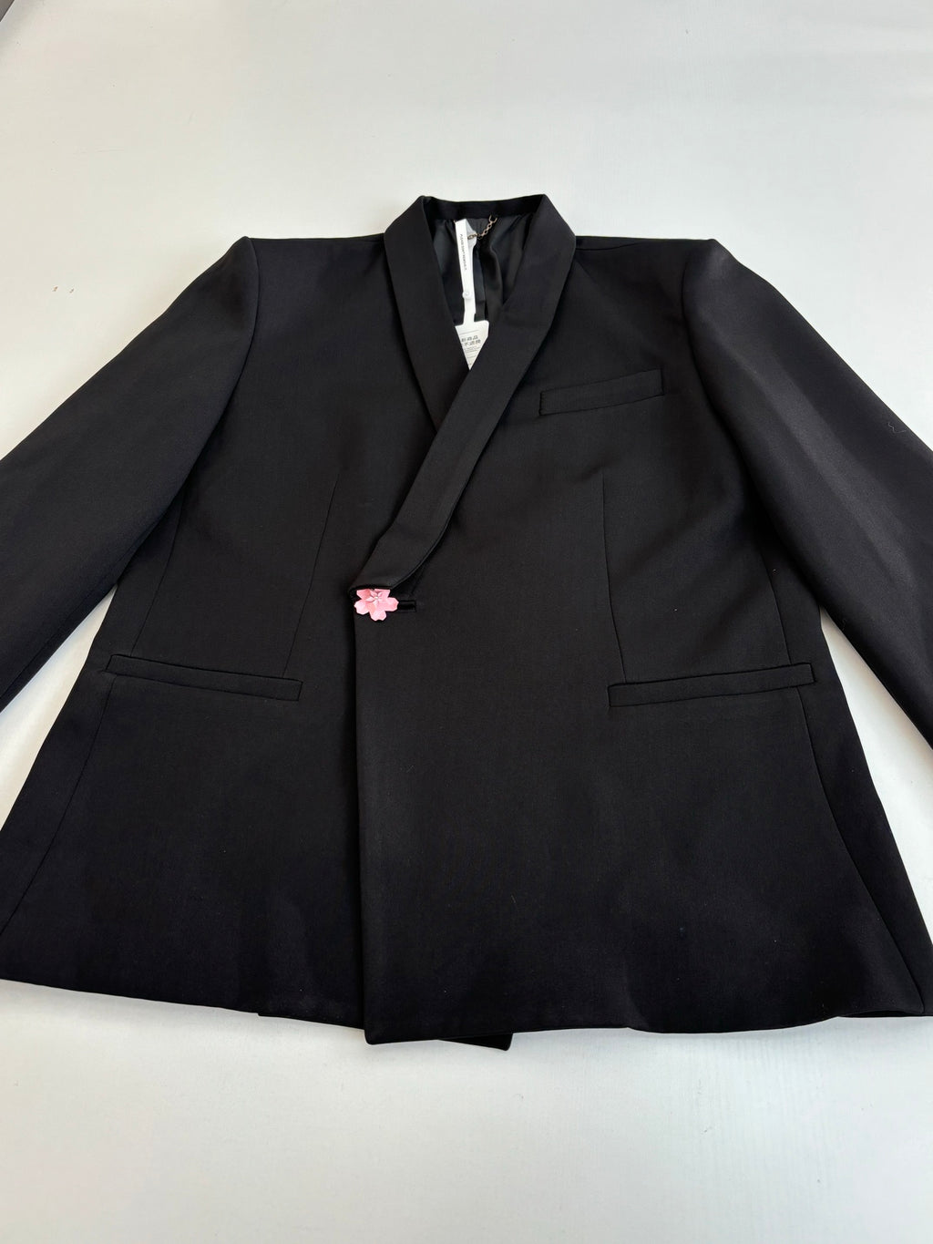 Black long blazer jacket with notch lapels and pink flower pin on the chest.