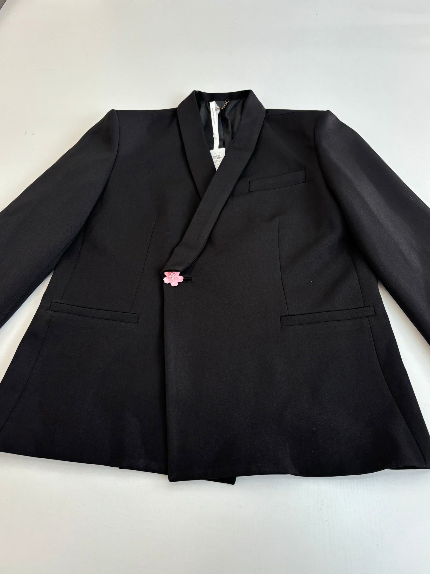 Black long blazer jacket with notch lapels and pink flower pin on the chest.