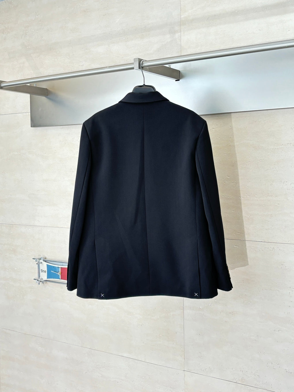 Black long blazer jacket back view with center seam, hanging on a hanger.
