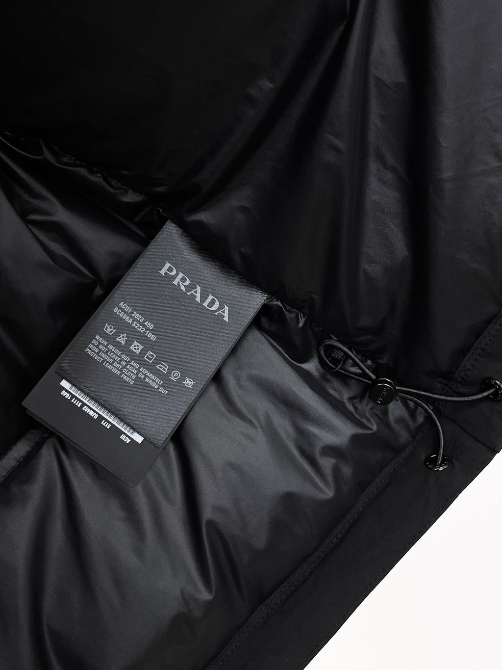 Dark puffer jacket fabric with Prada Milano care tag and drawstring detail