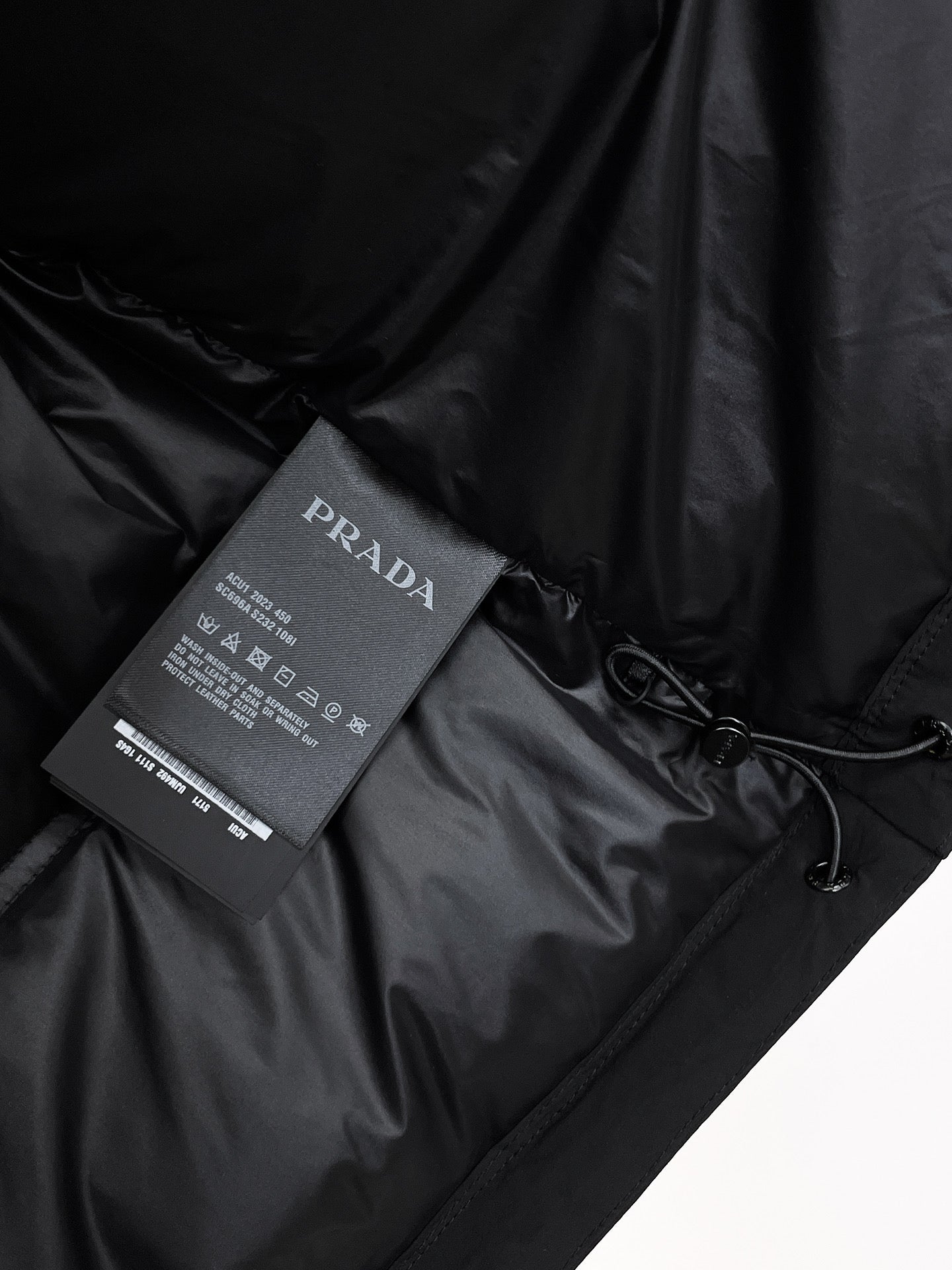 Dark puffer jacket fabric with Prada Milano care tag and drawstring detail