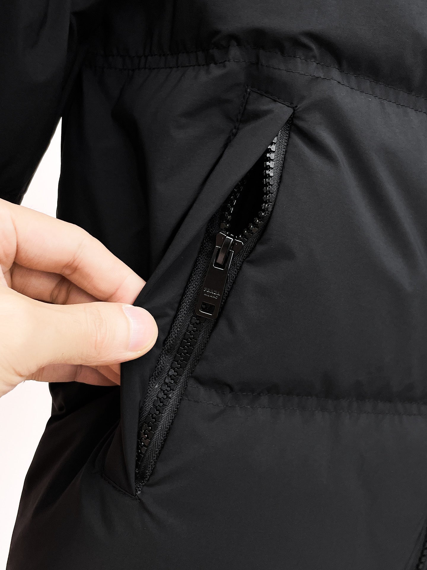 Hand pulling open a dark puffer jacket front zipper