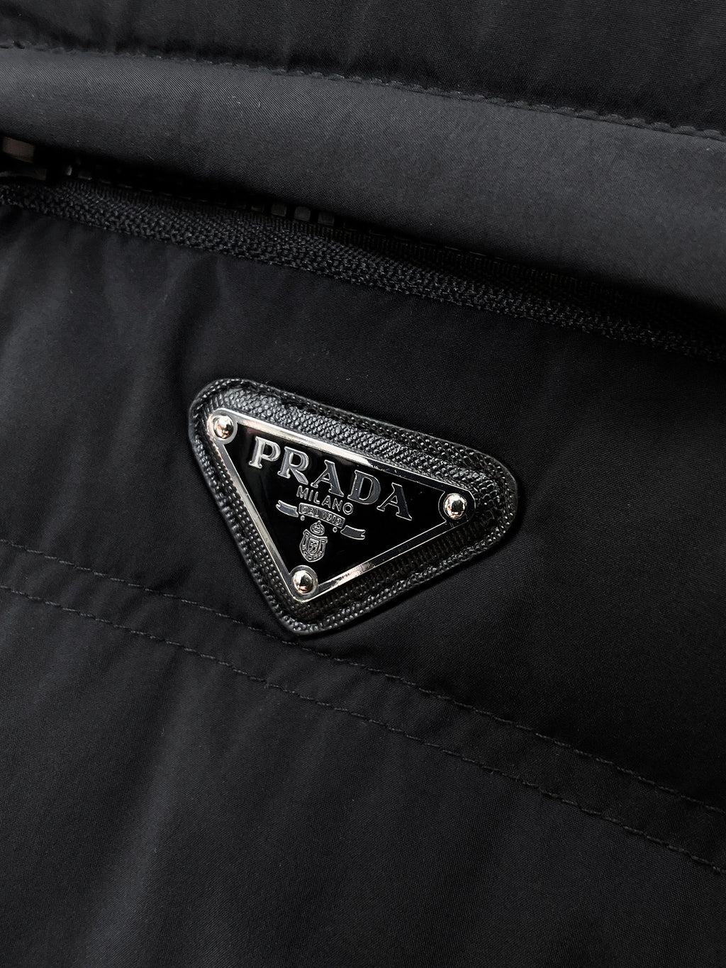 Prada Milano triangular logo patch on dark puffer jacket chest pocket
