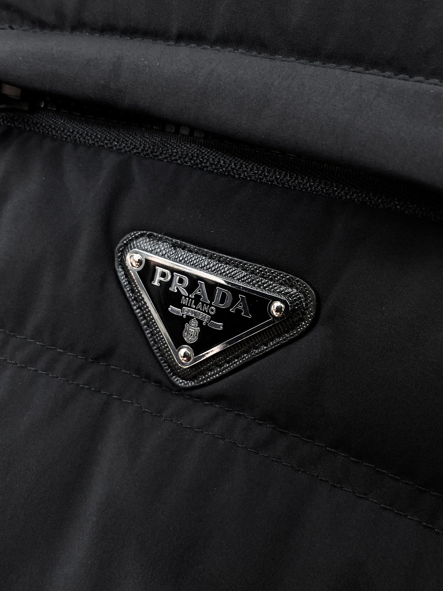 Prada Milano triangular logo patch on dark puffer jacket chest pocket