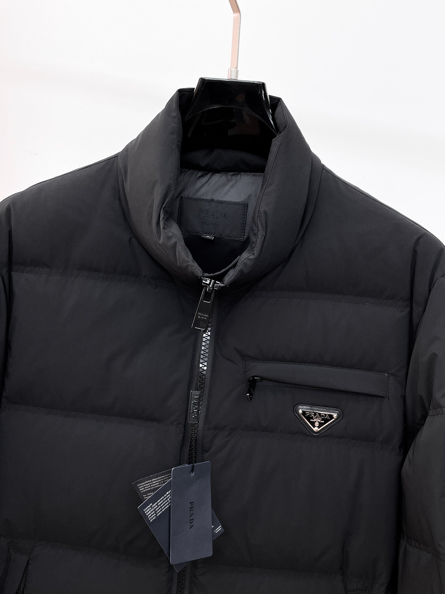 Dark long puffer jacket close-up: stand collar, front zipper, and triangular logo patch