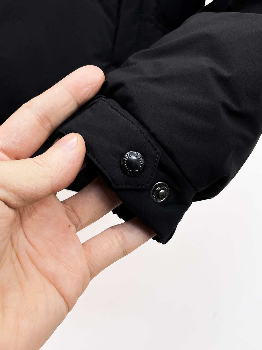 Dark puffer jacket cuff with snap button and ribbed inner trim