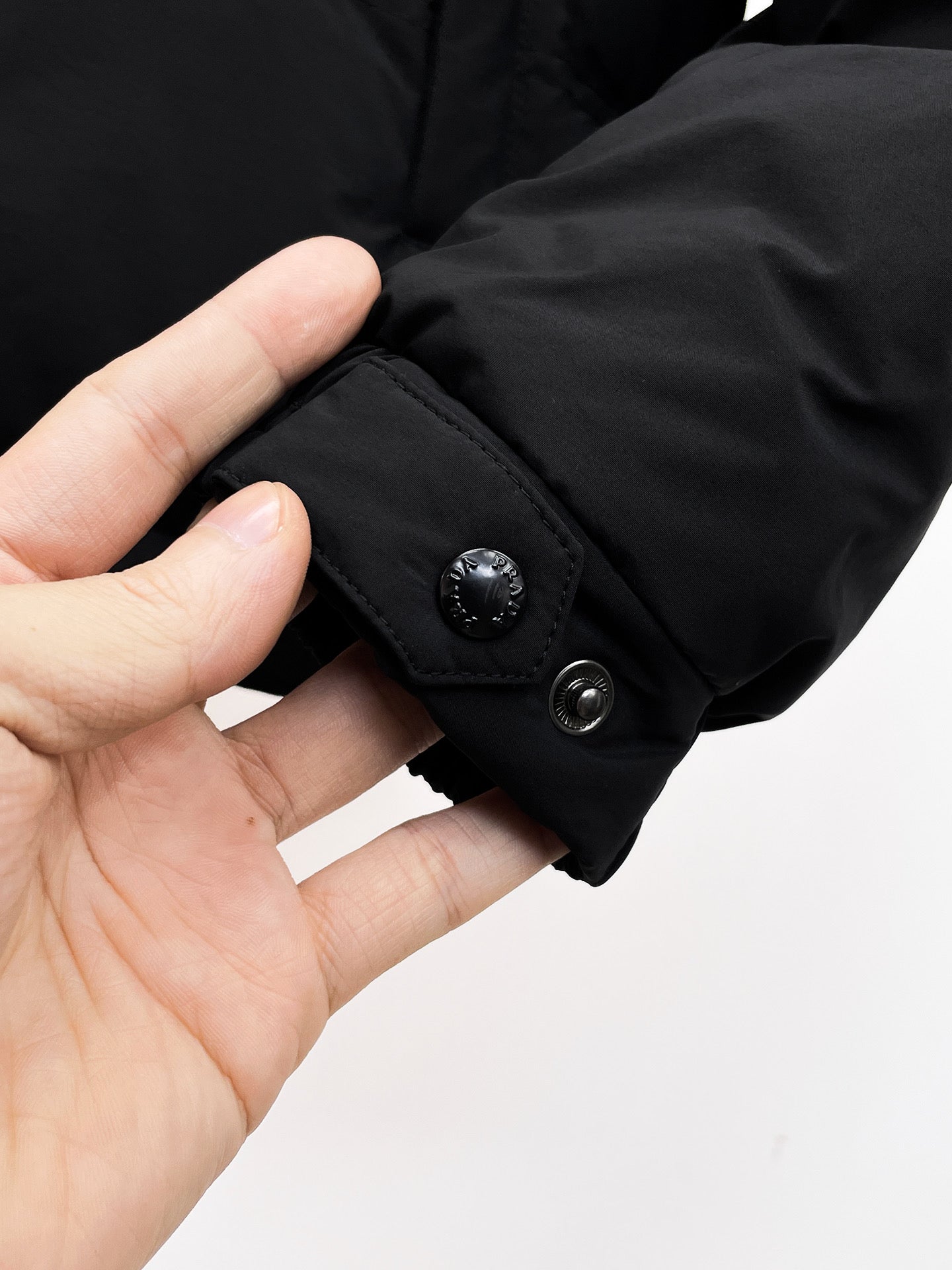 Dark puffer jacket cuff with snap button and ribbed inner trim
