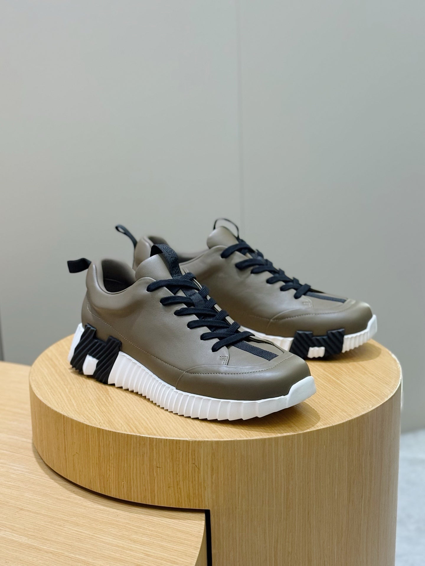 Olive sneakers with navy laces and white chunky soles on a round display