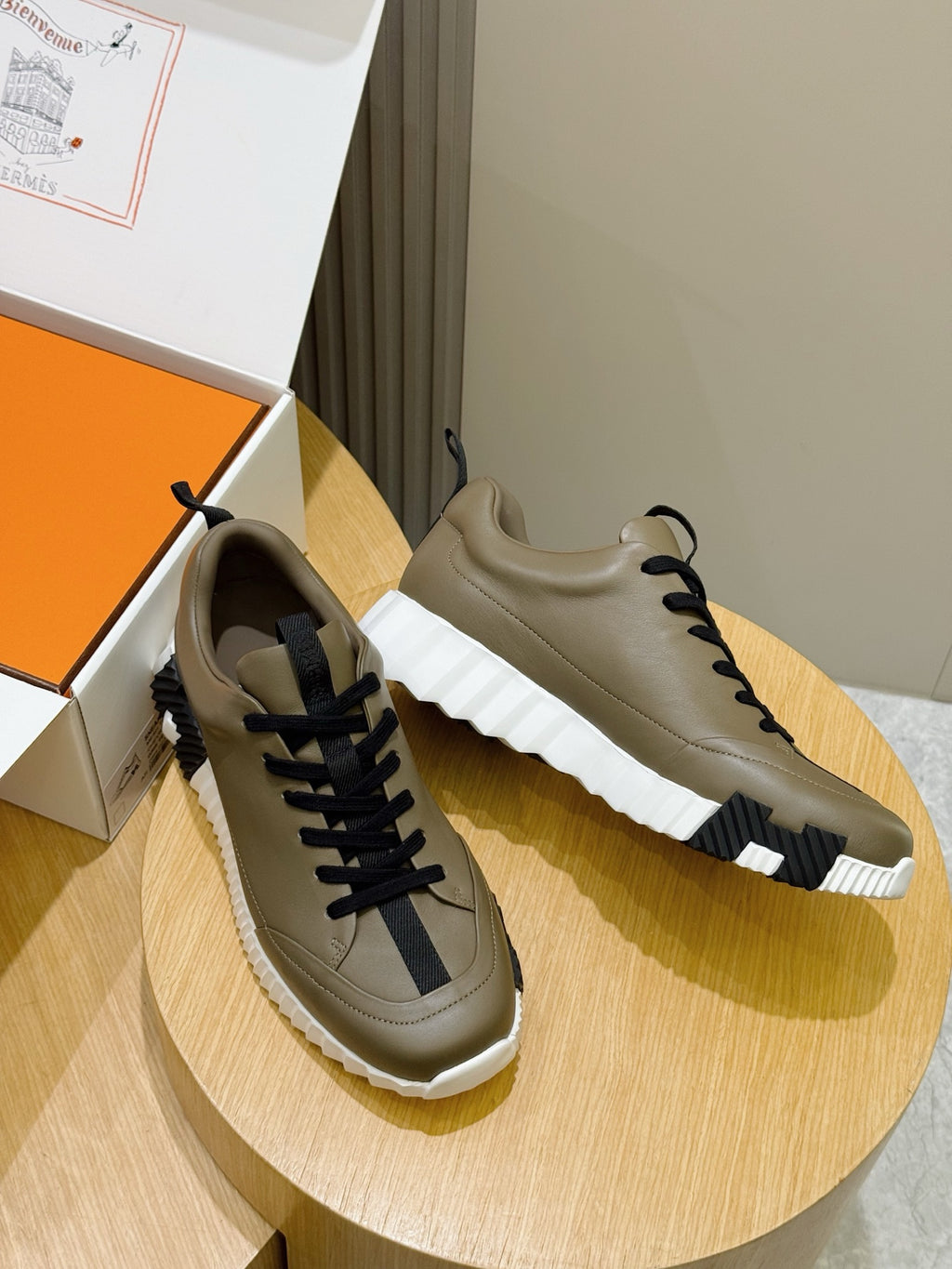 Pair of olive sneakers with navy laces and white soles on a round base